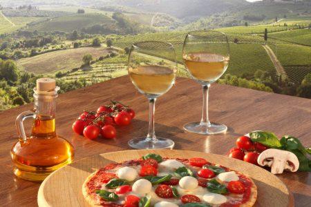 Italian pizza and glasses of white wine in Chianti, famous vineyard landscape in Italy